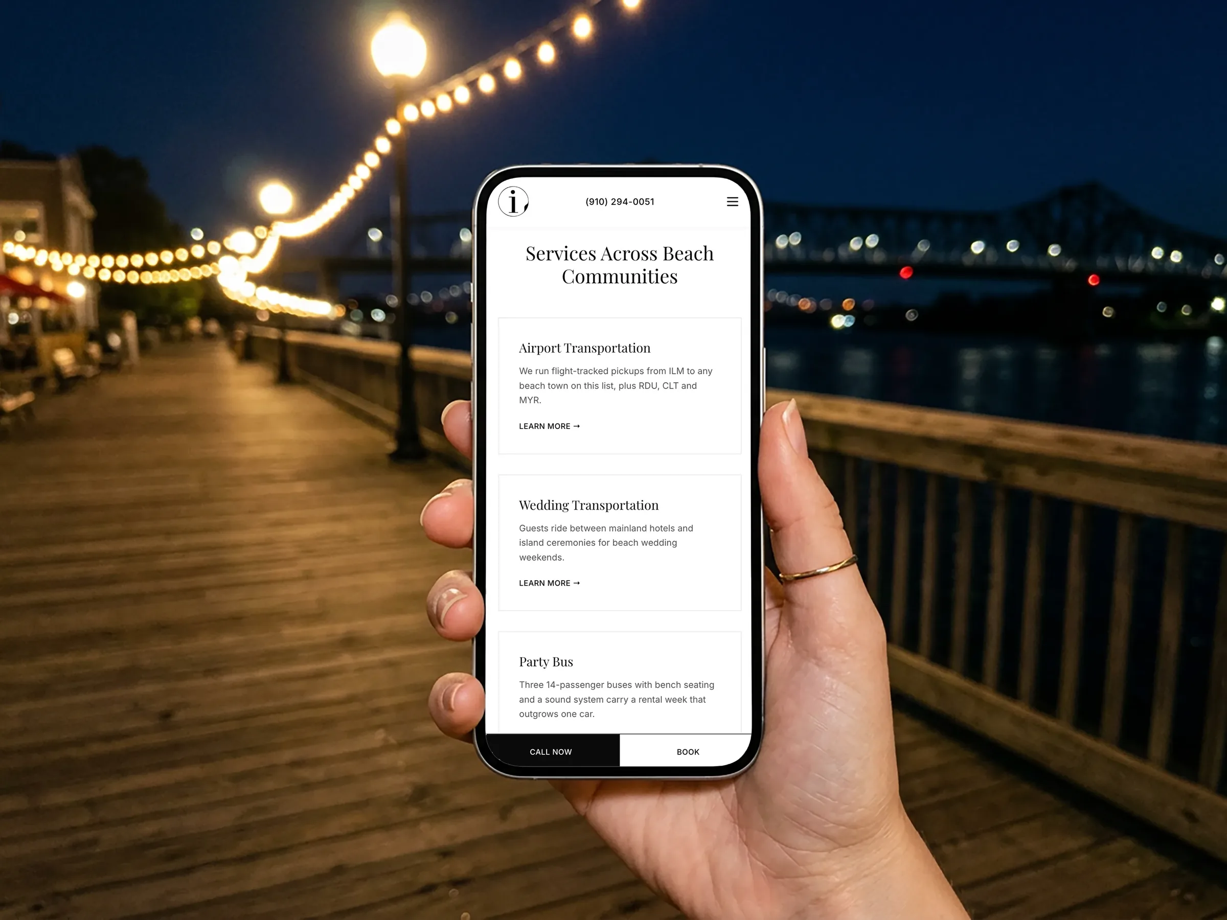 Icon Transportation Wilmington services page on a phone held up on the Wilmington riverwalk at night, listing airport, wedding and party bus transportation